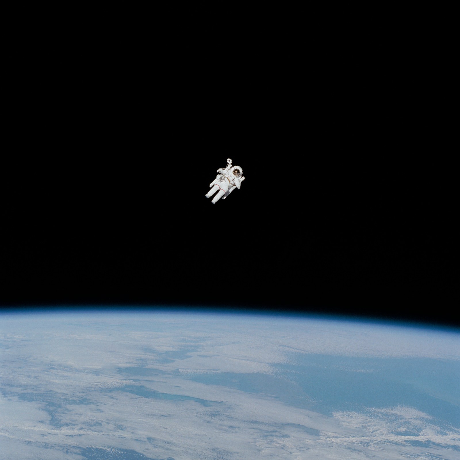A person in a white spacesuit appears to float alone above Earth